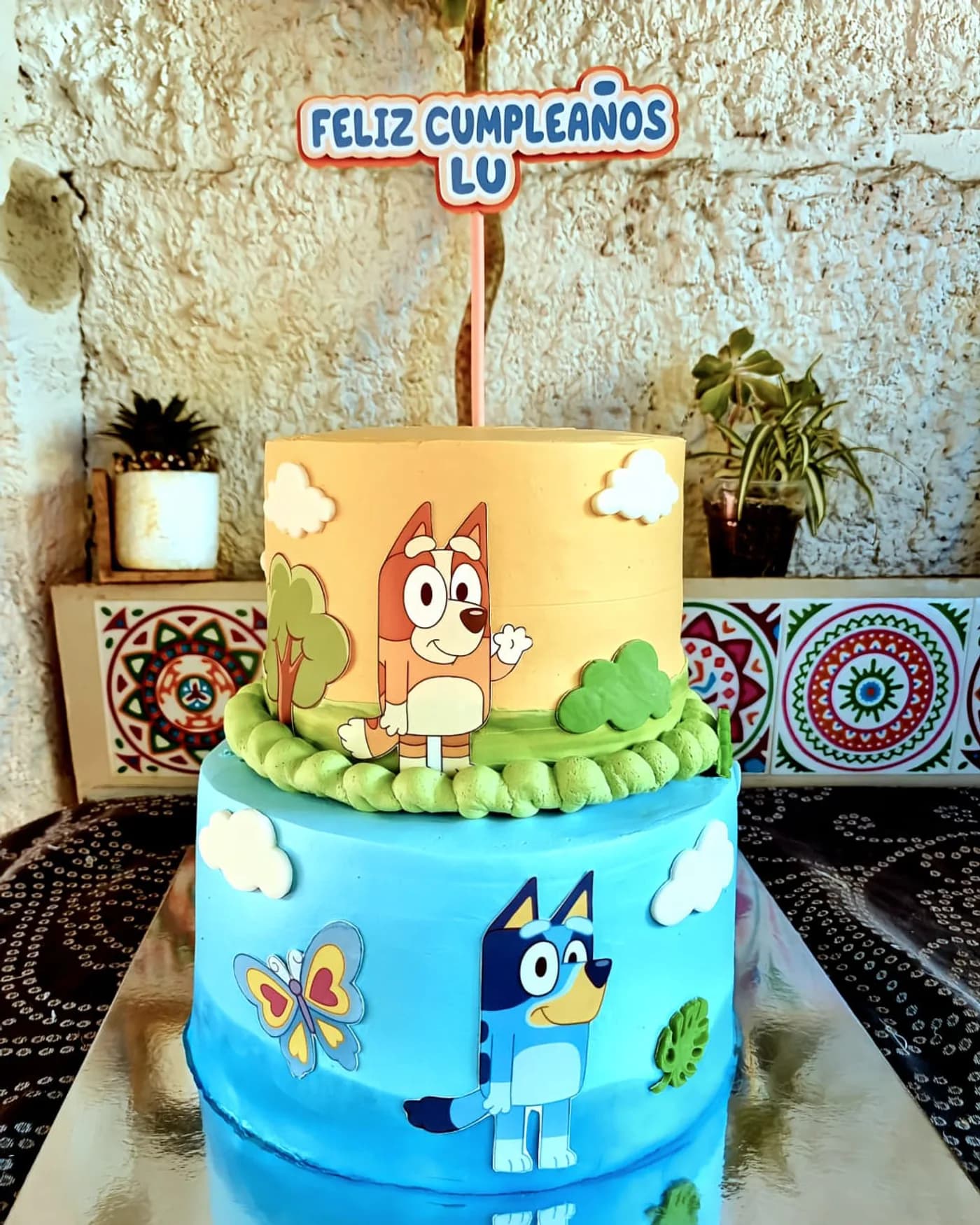 Torta de dos pisos celeste y naranja con personajes de Bluey en papel de azúcar