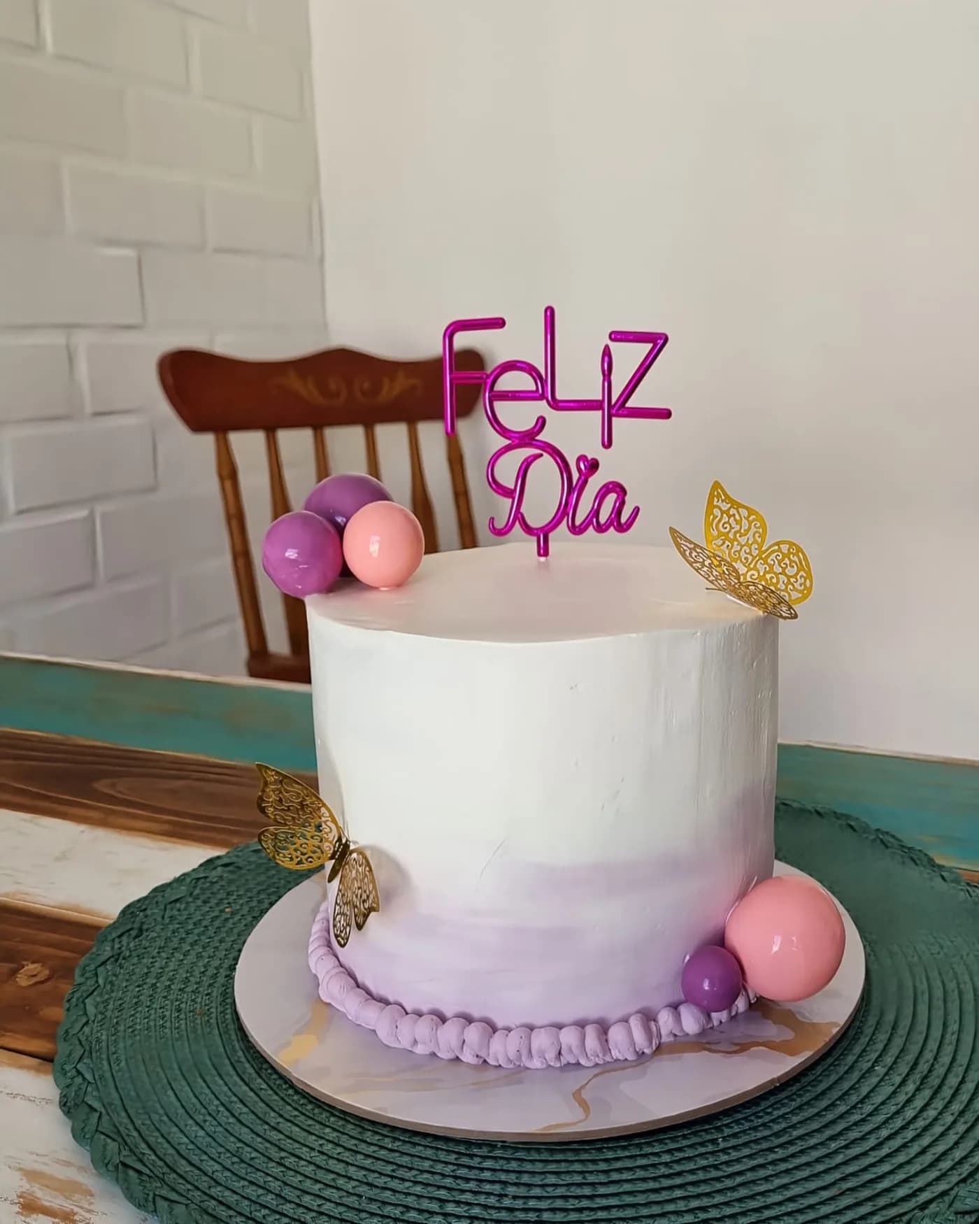 Torta minimalista con degradé blanco a lila, esferas de chocolate y mariposas doradas